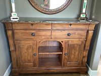 Front view of wooden sideboard with dark marble top, two drawers, two cabinets, and central open shelf.