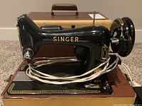 Close-up of the Singer sewing machine showing black body with gold lettering and decorative accents.