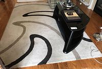 Full view of the beige area rug with black and taupe abstract curved designs and coffee table on top in a hardwood floor room.