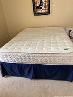 Full view of queen mattress and blue fabric box spring cover on bed frame.