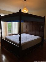 Full view of wooden four poster bed with white mattress, blue fabric canopy, and paneled design headboard and footboard.