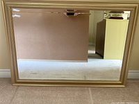 Front view of the rectangular mirror showing beveled edges and gold-tone faux wood frame.