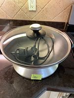 Full view of Breville electric wok with attached electric cord and temperature control inside, covered with glass lid on dark countertop.