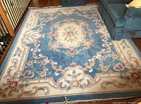 Top view of the large floral area rug laid on a hardwood floor with a blue sofa nearby.