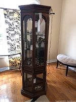 Full view of the tall wooden curio cabinet showing arched glass upper door, lower glass door, and hexagonal shape