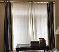 View of curtain panels hanging on the rod covering a window; one panel striped, one plain white, table below window.