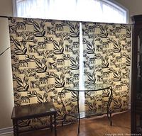Full view of two curtain panels covering a rectangular window area with part of a sheer demi lune visible above and items of furniture below