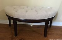 Side angle photo showing demi lune shape, beige tufted upholstery, and dark wood legs and base of the hall bench.