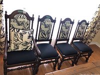 Four wooden and fabric dining chairs, one captain's chair with armrests and three regular chairs. All have black seats and black and white patterned cushions on the backs.