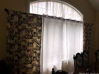 Full view of draped window showing black and white patterned drapes, white sheers, and curtain hardware.