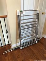 Folded adjustable drying rack with metal rods and white plastic parts leaning against door
