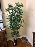 Full view of the 68-inch tall faux bamboo plant with multiple stalks and green leaves in a black pot, shown next to furniture for scale.