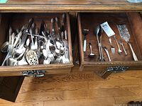 Two open drawers of silver plate flatware showing a large number of pieces including serving spoons, forks, and specialty utensils with ornate handles.