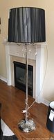 Full view of the chrome base floor lamp with black fabric shade and hanging crystal lustres, situated on hardwood floor near fireplace.
