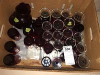 Box containing approximately 29 pieces of ruby glassware of various sizes and types including jars, drinking glasses, and smaller vessels, with some pieces having price tags.