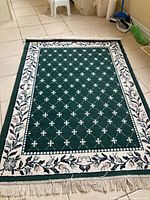 Full view of the rectangular green polyester area rug with white and pink floral border and white geometric pattern.