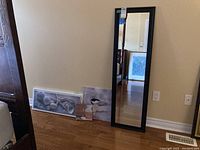Full view of the mirror and wall art leaning against wall on a wooden floor