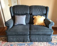 Front view of blue-green La-Z-Boy recliner loveseat with two cushions and two throw pillows (yellow and gray). Wingback design and padded arms visible.