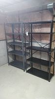 Two black metal shelving units standing side by side in a basement area, against unfinished pink insulation wall, showing overall view.