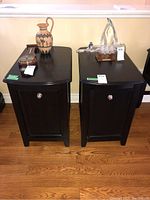 Front view of two matching dark wood side tables with items on top (not included).