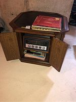 Front view of the octagonal stereo cabinet table showing open doors revealing built-in radio with controls and vinyl record storage underneath, topped with a stack of LP records.