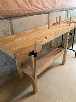Angled front view showing butcher-block style top, four square legs, lower shelf, and vise on left end.