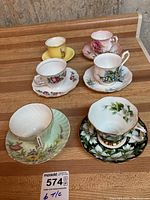 Six teacups and matching saucers arranged on wooden surface showing variety of floral designs and colors.