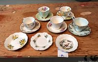 View of all five teacups with their matching saucers and three small dishes arranged on a wooden surface, showing design and condition.