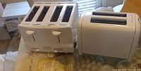 Two white Proctor Silex toasters, one 3-slice and one 2-slice, viewed from front showing slots and controls.