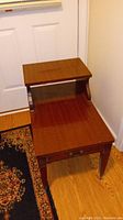Photo of one dark brown wooden end table showing the two-tier design, drawer with handles, and wheels