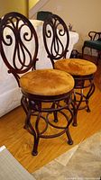 Two wrought iron swivel base bar stools with mustard brown suede round seats, used indoors on wood flooring.