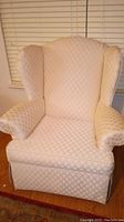 Front view of a wingback chair upholstered in off white diamond patterned fabric.