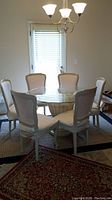Dining set in room showing round glass top table with six beige/off white upholstered chairs.