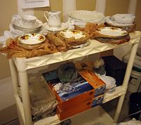 Two shelves holding wrapped china sets with floral patterns and boxed crystal trays and glasses below