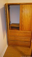 Light brown wooden TV armoire showing the open TV compartment, upper shelf, right cabinet door, and four lower drawers.