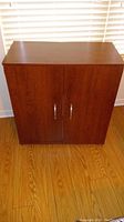Front view of the dark brown wood cabinet with two doors and silver handles.