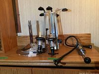 Bar dispenser set including a stainless steel base with multiple vertical clear plastic measuring or bottle holder devices with black fittings and a multi-part assembly with chrome and black components on a wooden surface