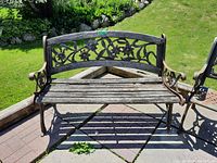 Front view of the outdoor bench showing wood seat slats and floral detailed metal backrest and armrests