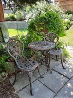 Front view of two chairs and round table outdoors on pavers with surrounding garden