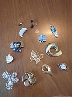Overhead photo showing the full collection of brooches and pins on wooden surface, variety of shapes and sizes including butterfly, floral, dog, cameo, and abstract shapes.