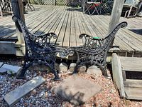 Two cast iron bench ends placed side by side outdoors with visible ornate floral and leaf pattern details.