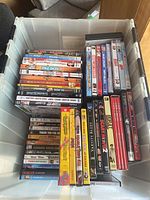 Photo showing a bin filled with assorted DVDs stacked horizontally and vertically to show spines and covers.