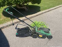 Side view of electric lawn mower with grass catcher bag and one green extension cord coiled on ground.