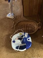 View of foot spa and wicker basket on carpeted floor, showing power cord and handles on basket.