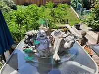 Clear view of multiple garden decor items on glass table including Buddha, turtle, frog, small figures, and other decorative pieces.