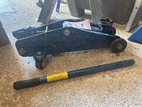 Blue hydraulic floor jack with handle lying next to it on garage floor.