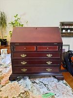 Front view of wood jewelry cabinet showing 5 visible drawers and a fold-down door panel closed.