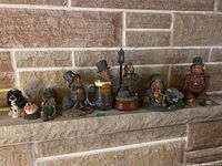 Photo shows eight decorative leprechaun figurines lined up along a stone wall, featuring varied themes including a dog, beer mug, lantern, and musical instruments.