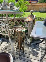 Photo showing two metal plant stands and the tall metal candle holder on a wooden deck with outdoor furniture.