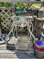 Photo showing white metal plant stand with decorative front and lattice shelf, various metal plant pots stacked on right side.